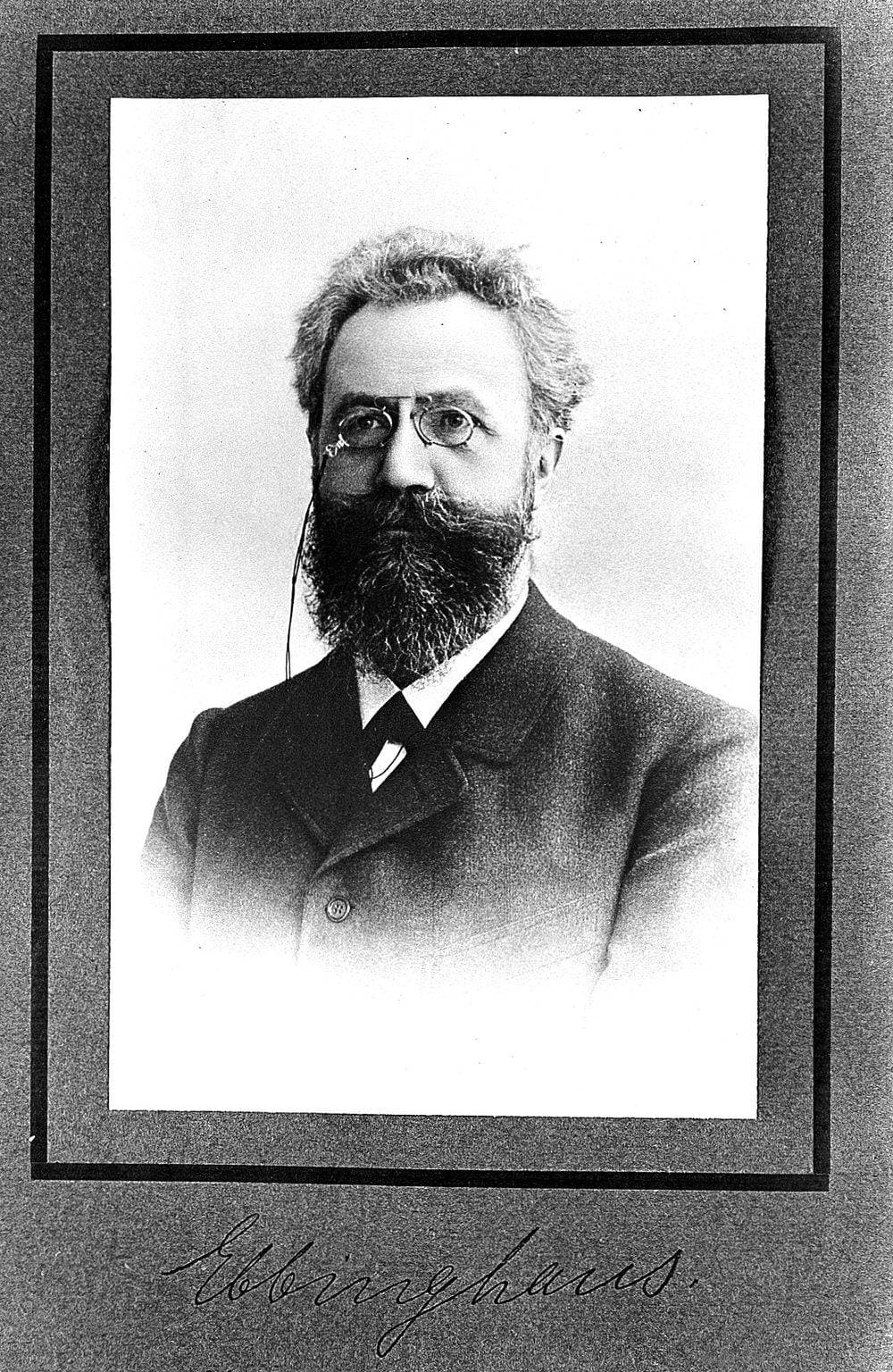 Retrato fotográfico de Hermann Ebbinghaus, de óculos e barba cheia, com a assinatura dele embaixo.