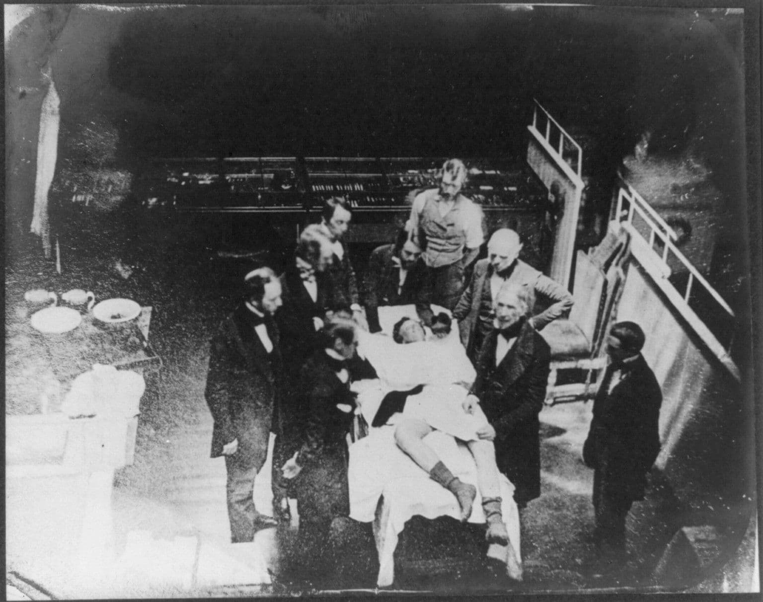 Fotografia antiga de uma sala de operação, com a mesa e os instrumentos.